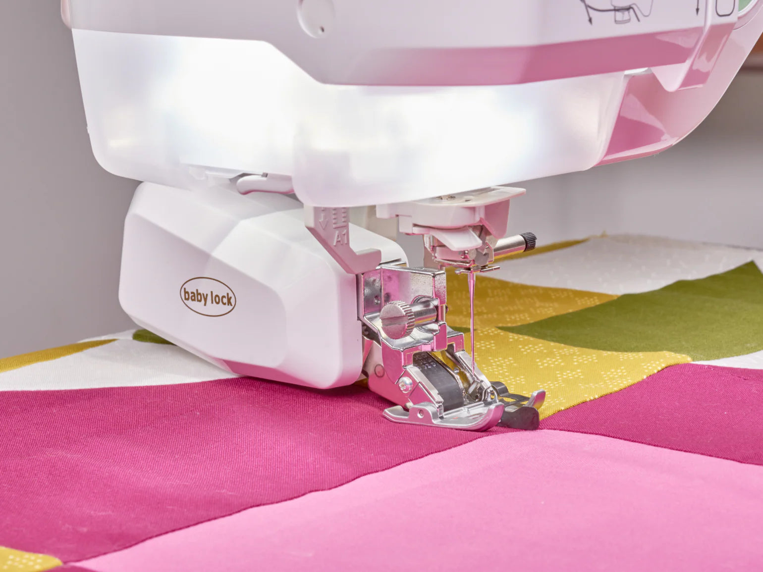A close-up of the Baby Lock Anthem Sewing & Quilting Machine with FREE 60 Days of Online Classes, featuring StitchSync Regulation as it stitches vibrant pink, green, and yellow fabrics from a colorful quilting bundle.