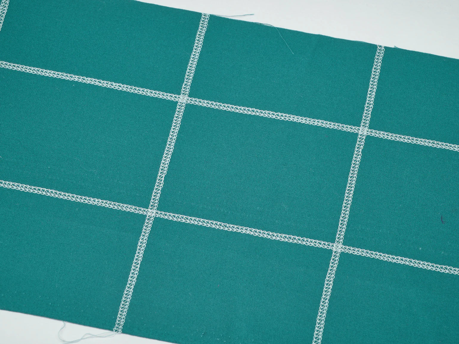 Teal fabric featuring intersecting white stitched lines in a grid pattern, ideal for use with the Baby Lock Splendor 8-Thread Combination Serger with ExtraordinAir™ Threading and FREE 60 days of online classes.