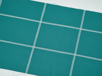 Teal fabric featuring intersecting white stitched lines in a grid pattern, ideal for use with the Baby Lock Splendor 8-Thread Combination Serger with ExtraordinAir™ Threading and FREE 60 days of online classes.