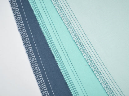 Four blue and aqua fabric pieces are stacked diagonally, showing their stitched edges finished with the Baby Lock Splendor 8-Thread Combination Serger with ExtraordinAir™ Threading on a white background. Includes 60 days of free online classes.