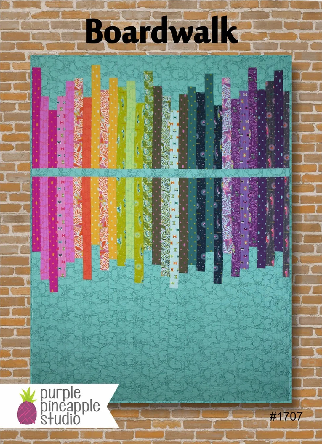 The Boardwalk Quilt Pattern by Purple Pineapple Studio features vertical rainbow strips on a turquoise background. Perfect for showcasing your favorite jelly roll fabrics, it's shown as a colorful quilt hanging on a brick wall.