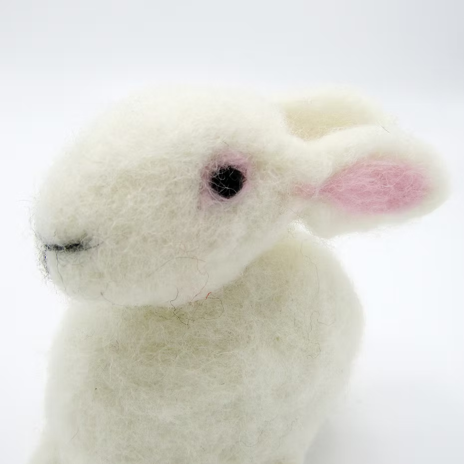 A close-up of a white felted bunny with black eyes, pink inner ears, and a stitched mouth, created using the Feather Felts Bunny - Needle Felting Kit No Foam, displayed on a plain white background.