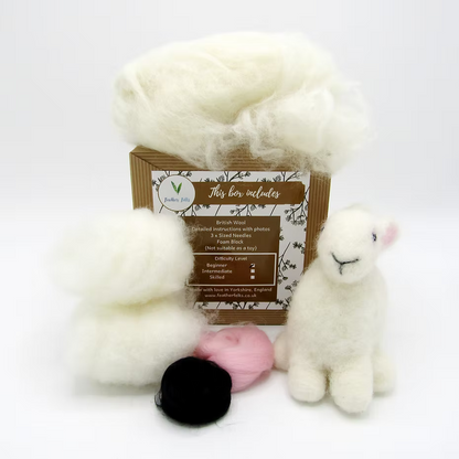 The Feather Felts Bunny Needle Felting Kit (No Foam) includes British wool, two wool bundles, small balls of black and pink wool, and a finished felted bunny with a smiling face—all neatly arranged around the box.