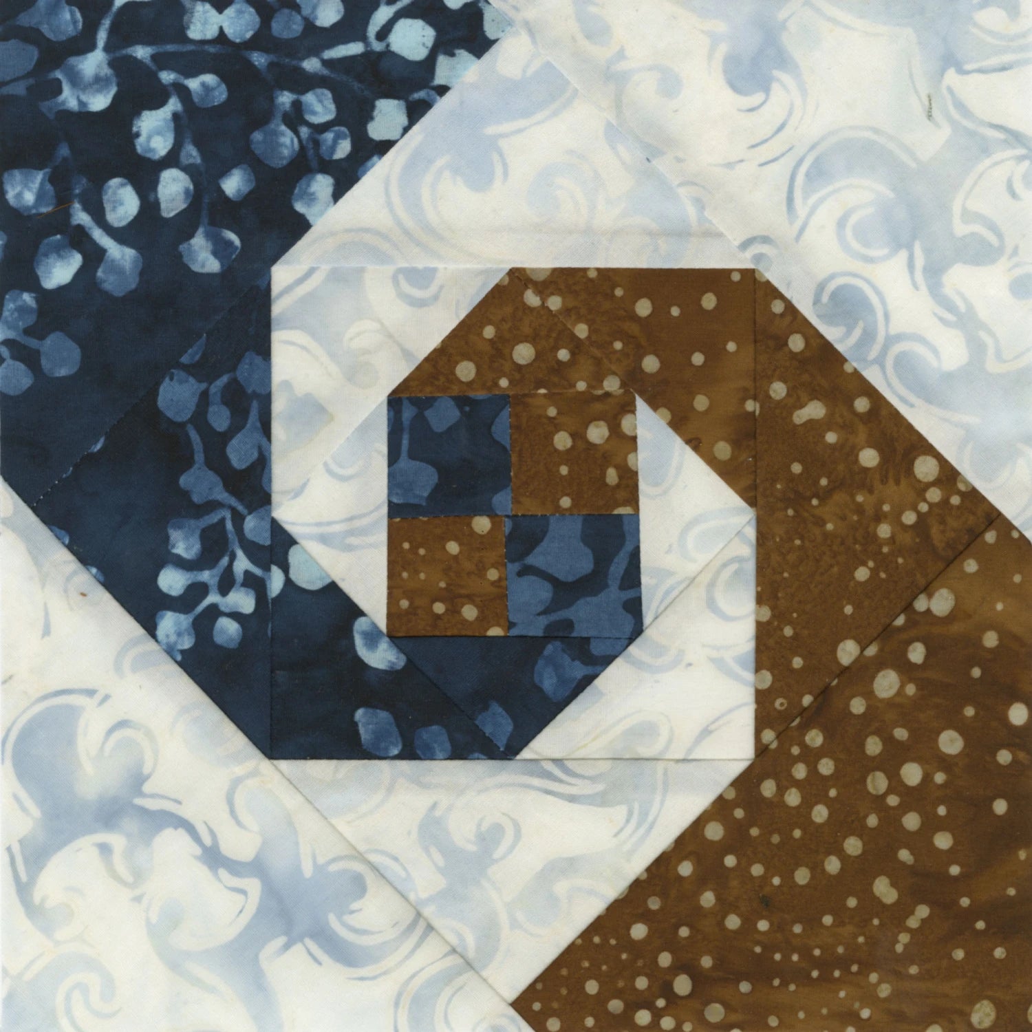 Create precise quilt blocks with spiral designs using blue, brown, and white patterned fabrics by trimming with the Checker Distributor Creative Grids Square on Square Trim Tool for 4in or 8in finished blocks.