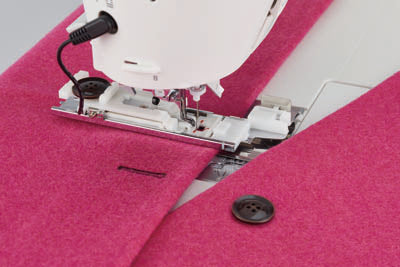 A buttonhole being sewn by the JUKI Hayate DX-4500QVP in bright pink felt, with a black button placed beside it.