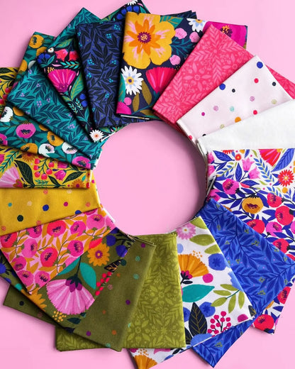 A circular display of the Dayspring Fat Quarter Bundle by Windham Fabrics shows vibrant floral, geometric, and polka dot quilting fabrics in blue, pink, green, yellow, and white on a pink background.
