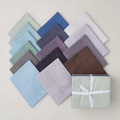 A selection of neatly arranged fabric squares in various cool colors and subtle patterns, including the Crimp Cool Colors Fat Quarter Bundle by Dear Stella, with one bundle tied with a white ribbon, displayed on a light surface.