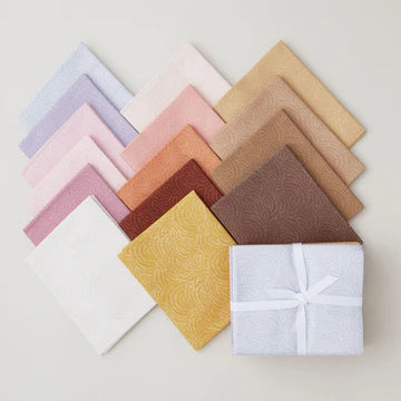 The Dear Stella Crimp Warm Colors Half Yard Bundle features textured quilting fabrics in pastel and earth tones, displayed in a diamond pattern, with one piece folded and tied with a white ribbon in the lower right corner.