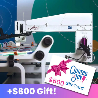 The APQS Freddie 26" Quilting Machine with Comfort Lift Table is pictured quilting a colorful quilt, with a Quilted Joy $600 gift card wrapped in a pink ribbon in the foreground. Below, bold text reads +$600 Gift! on a purple background.