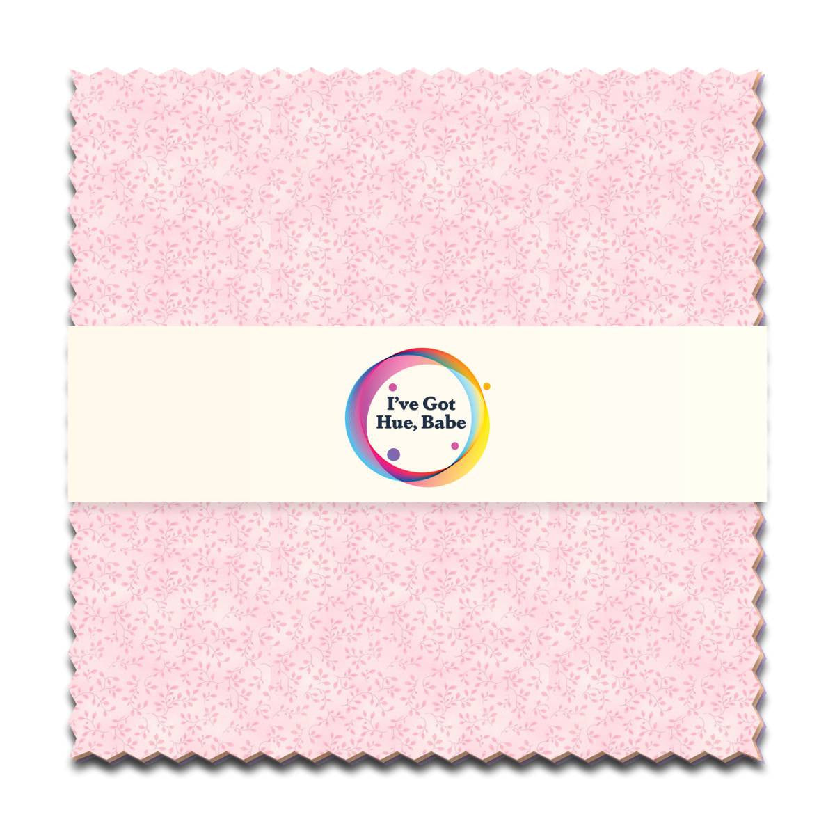 A 5" square swatch of light pink patterned fabric from Jaftex - Henry Glass Fabrics’ “I've Got Hue, Babe Light as a Feather” is wrapped with a white paper band featuring a colorful logo—ideal for charm pack or quilt projects.