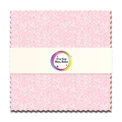A 5" square swatch of light pink patterned fabric from Jaftex - Henry Glass Fabrics’ “I've Got Hue, Babe Light as a Feather” is wrapped with a white paper band featuring a colorful logo—ideal for charm pack or quilt projects.