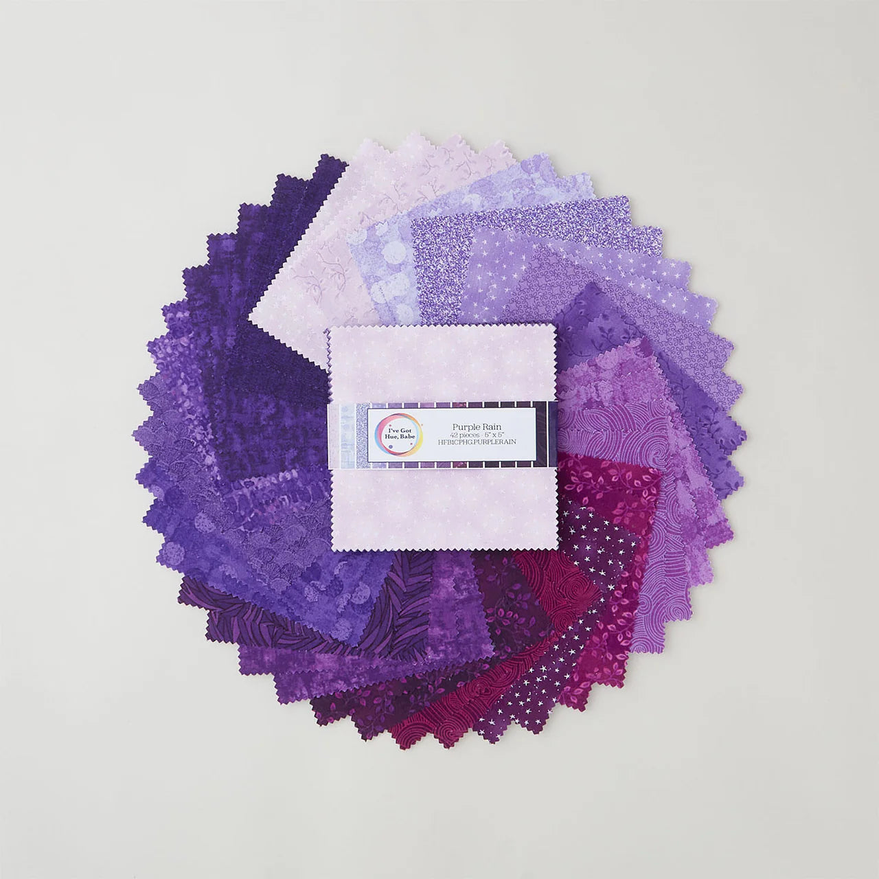 A circular display of Jaftex - Henry Glass Fabrics "I've Got Hue, Babe Purple Rain 5" Squares" features precut fabrics in shades from light lavender to deep violet on a light background, with the labeled charm pack bundle at the center.