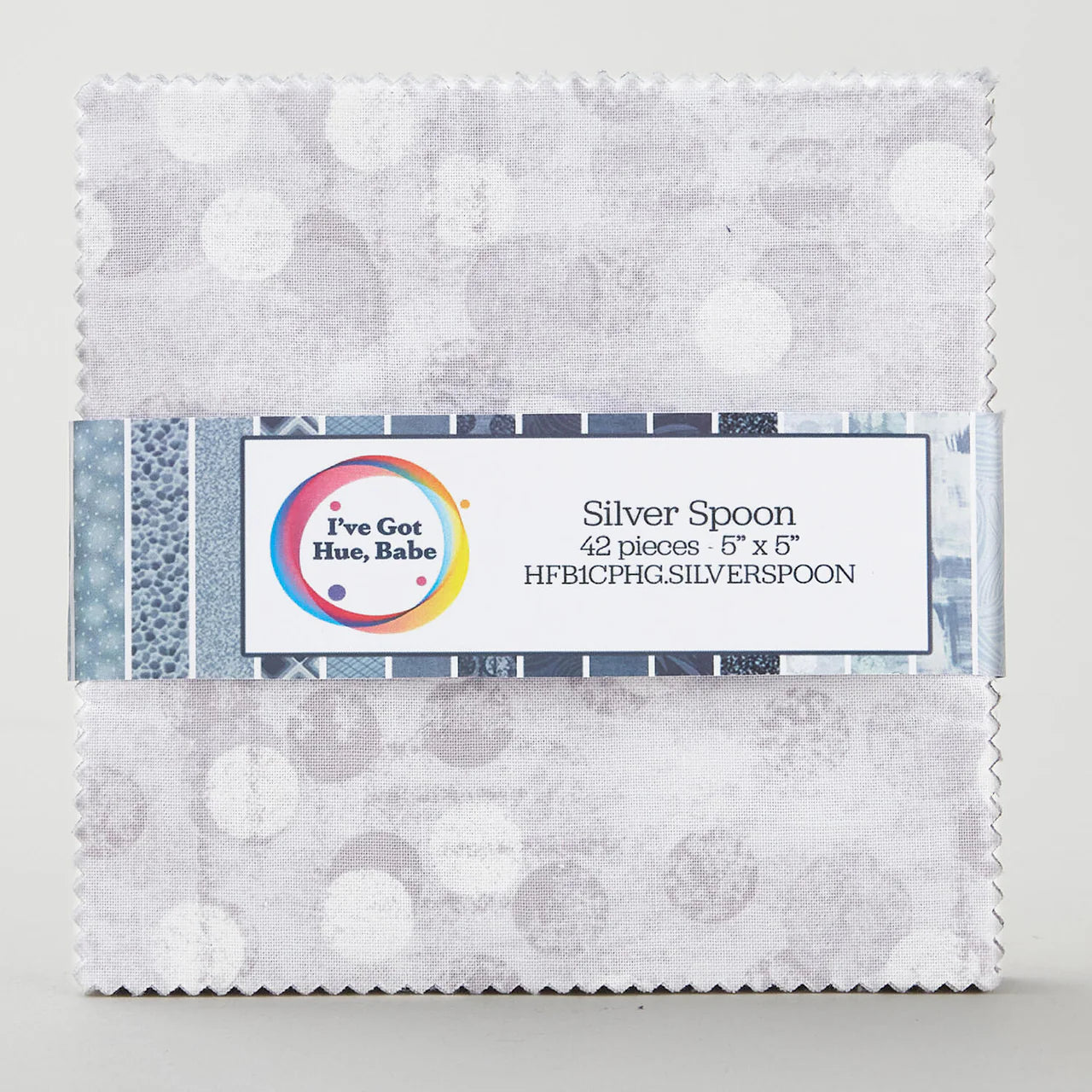 A charm pack of 5" squares, I've Got Hue, Babe Silver Spoon by Jaftex - Henry Glass Fabrics, featuring grey and white circle patterns, is neatly stacked and wrapped with a product info label.