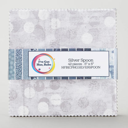 A charm pack of 5" squares, I've Got Hue, Babe Silver Spoon by Jaftex - Henry Glass Fabrics, featuring grey and white circle patterns, is neatly stacked and wrapped with a product info label.