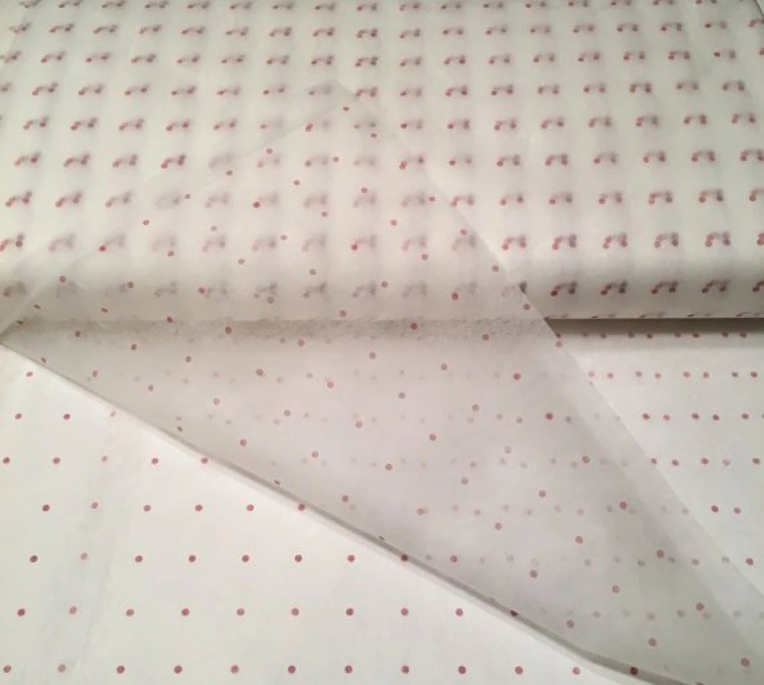 The Checker Distributor 25 Yard Bolt of Red Dot Tracer Tracing Material, White, 46in Wide, is shown over matching white fabric with red dots to demonstrate precise alignment for garment alterations.