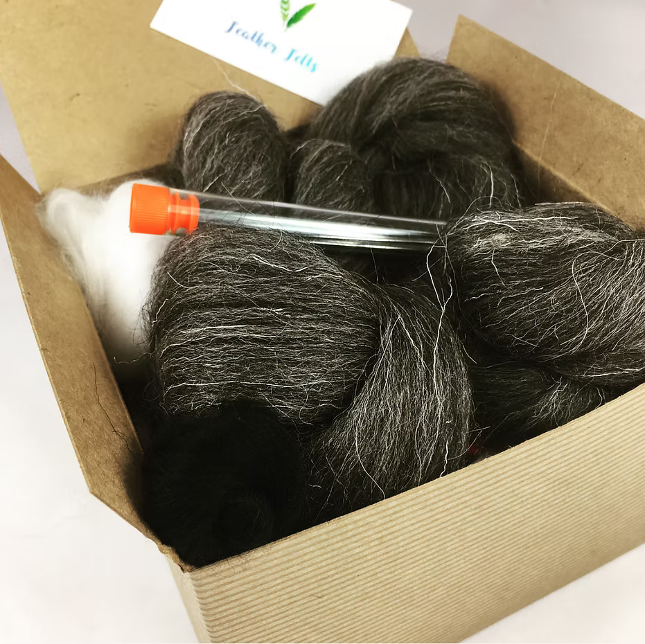 The Feather Felts Grey Hare - Needle Felting Kit No Foam includes bundles of dark and light gray wool, a small clear tube with an orange cap, and a partially visible white business card. Perfect for beginner needle felting.