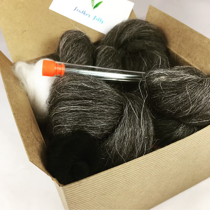 The Feather Felts Grey Hare - Needle Felting Kit No Foam includes bundles of dark and light gray wool, a small clear tube with an orange cap, and a partially visible white business card. Perfect for beginner needle felting.