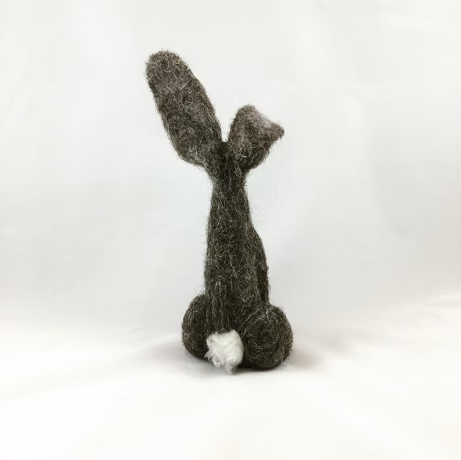 The Feather Felts Grey Hare - Needle Felting Kit (No Foam) features a handmade felted figure resembling a rabbit's back view with long ears and a small white tail, ideal for beginner needle felting against a plain white background.
