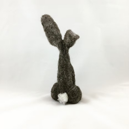 The Feather Felts Grey Hare - Needle Felting Kit (No Foam) features a handmade felted figure resembling a rabbit's back view with long ears and a small white tail, ideal for beginner needle felting against a plain white background.