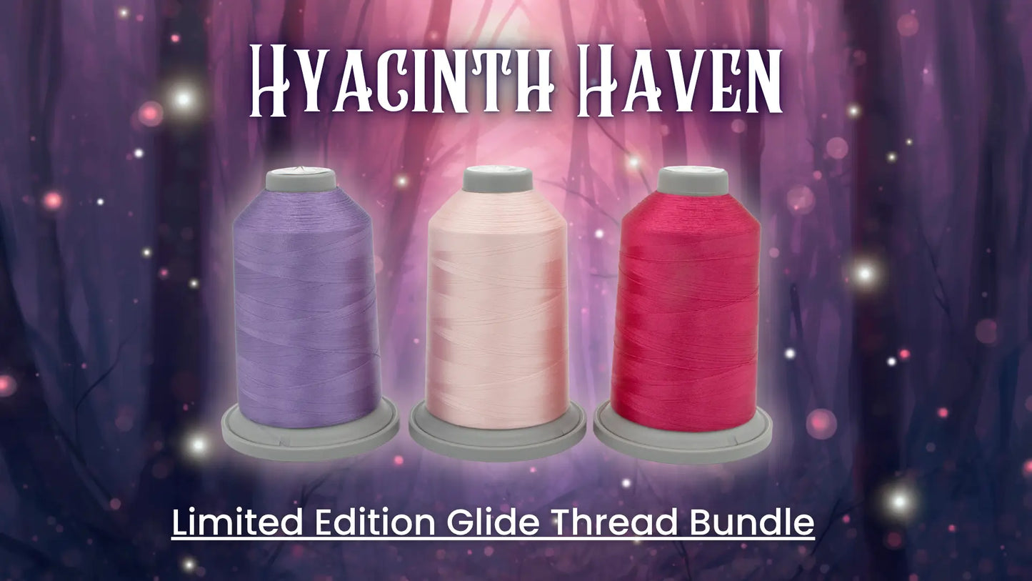 Three spools of Hab+Dash by Fil Tec's Hyacinth Haven Glide Thread of the Month Bundle in lavender, pale pink, and vibrant pink are set against a dreamy purple forest with "HYACINTH HAVEN" above and "Limited Edition Glide Thread Bundle" below.