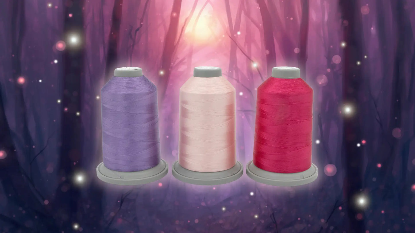 Three spools from the Hyacinth Haven Glide Thread of the Month Bundle by Hab+Dash by Fil Tec—lavender, pale pink, and bright pink—rest in a mystical forest scene, ideal quilting or embroidery thread for your next magical project.