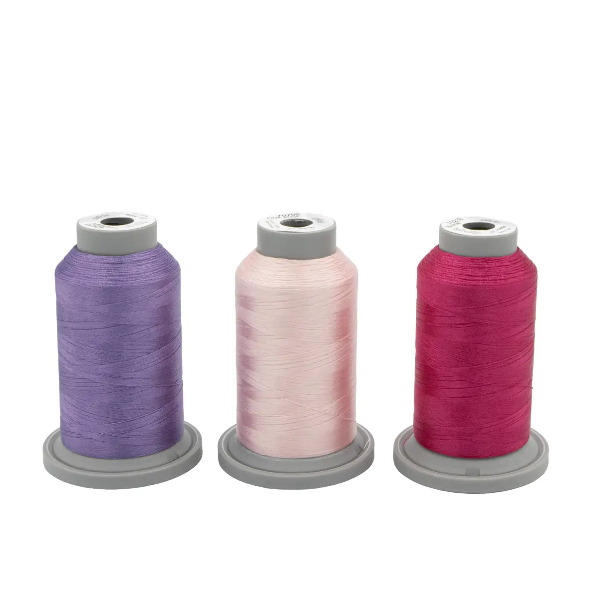 The Hyacinth Haven Glide Thread of the Month Bundle by Hab+Dash by Fil Tec features three spools—purple, light pink, and dark pink on gray bases—ideal for embroidery or quilting, all displayed side by side against a white background.