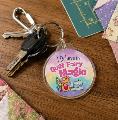 The Quilt Fairy Magic Keychain by Checker Distributor features a round charm with "I Believe in Quilt Fairy Magic," a cute cartoon fairy, and sewing machine—an adorable quilting accessory for any crafter.