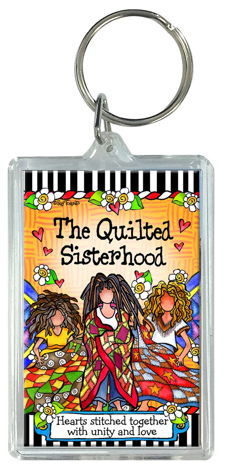 The Quilt Sisterhood Keychain by Checker Distributor features three women in colorful quilts, with "The Quilted Sisterhood—hearts stitched together with unity and love" and a background of hearts, flowers, and vibrant patterns.