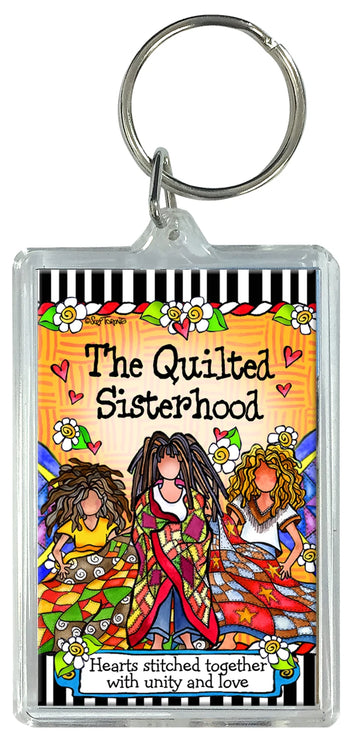The Quilt Sisterhood Keychain by Checker Distributor features three women in colorful quilts, with "The Quilted Sisterhood—hearts stitched together with unity and love" and a background of hearts, flowers, and vibrant patterns.