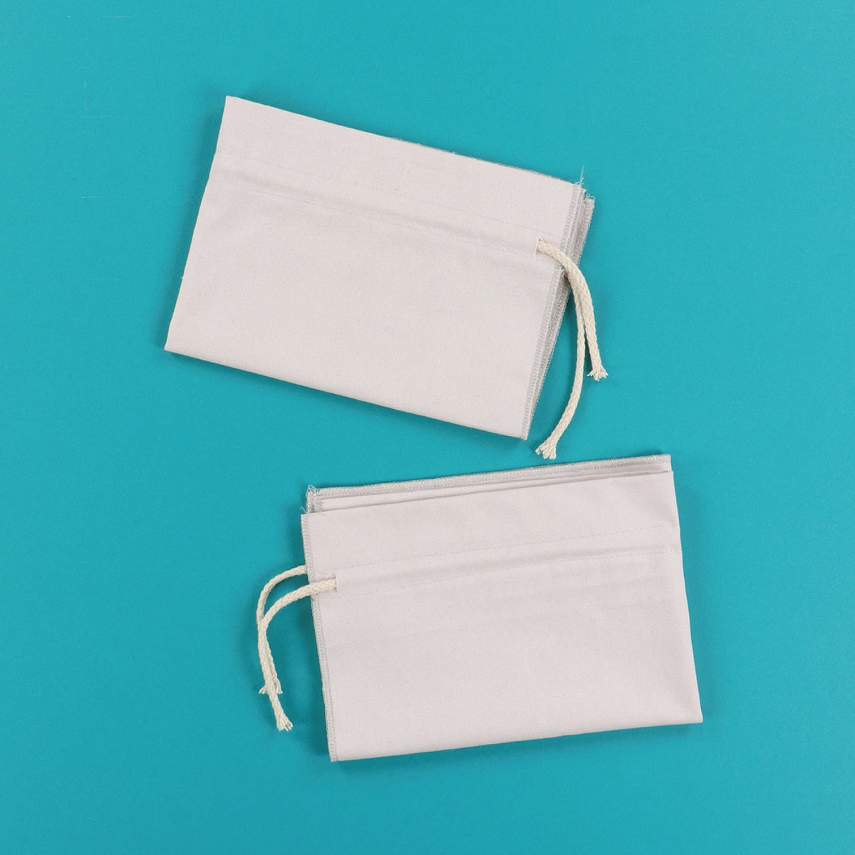 Two Kimberbell grey cinch sacks with drawstring closures on teal background