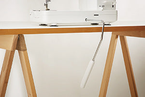 The knee lifter lever of the JUKI Haruka TL-18QVP fitted under the machine bed on a trestle sewing table.
