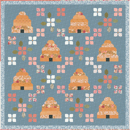 The Bloom & Buzz Quilt Pattern features a blue background with vintage patchwork of orange beehives, white and pink flowers, and green leaves, finished with a floral blue and white trim—perfect to add farmhouse charm to any space.