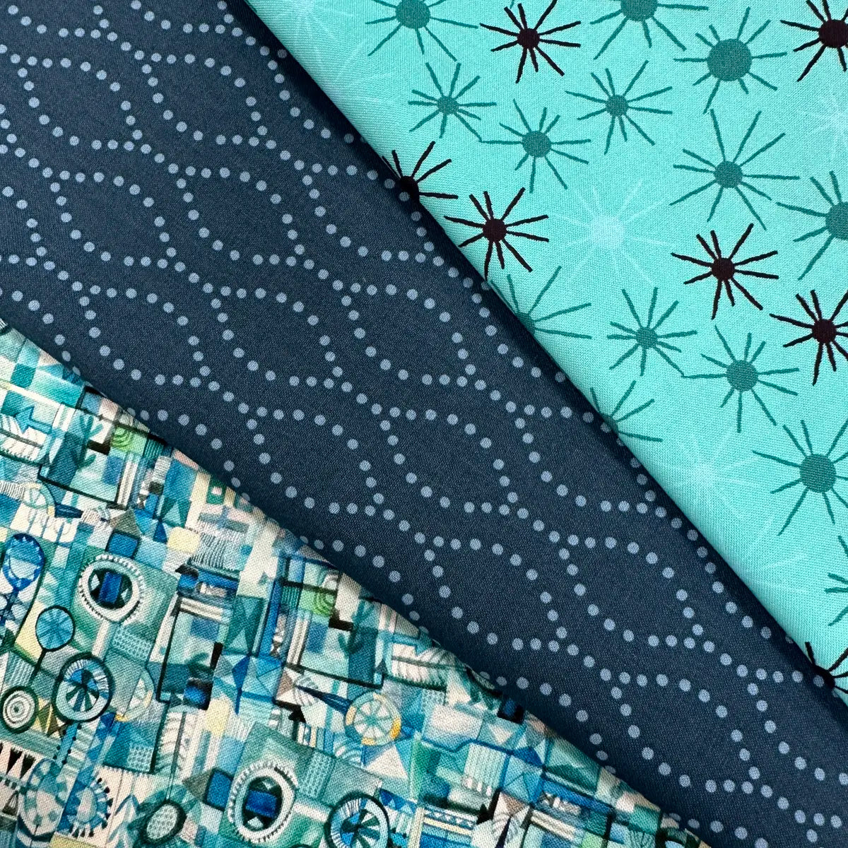 The Quilted Joy L'Heure Bleue Mint 3 Yard Quilt Top Bundle includes three fabrics: light blue with dark starbursts, navy with dotted wavy lines, and blue, teal, and white geometric patchwork—ideal for your next quilting project!.
