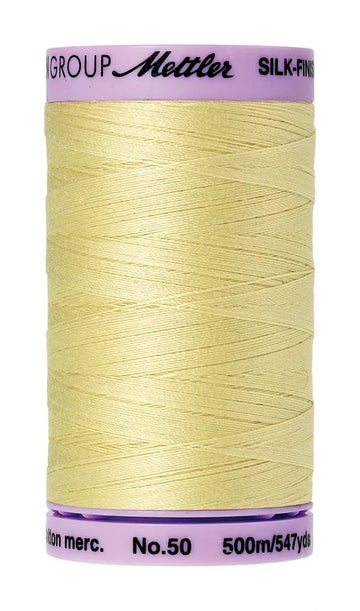 A spool of Mettler Cotton Silk Finish 50wt 500m sewing thread in Lemon Frost, with a pale yellow color and pale pink label.