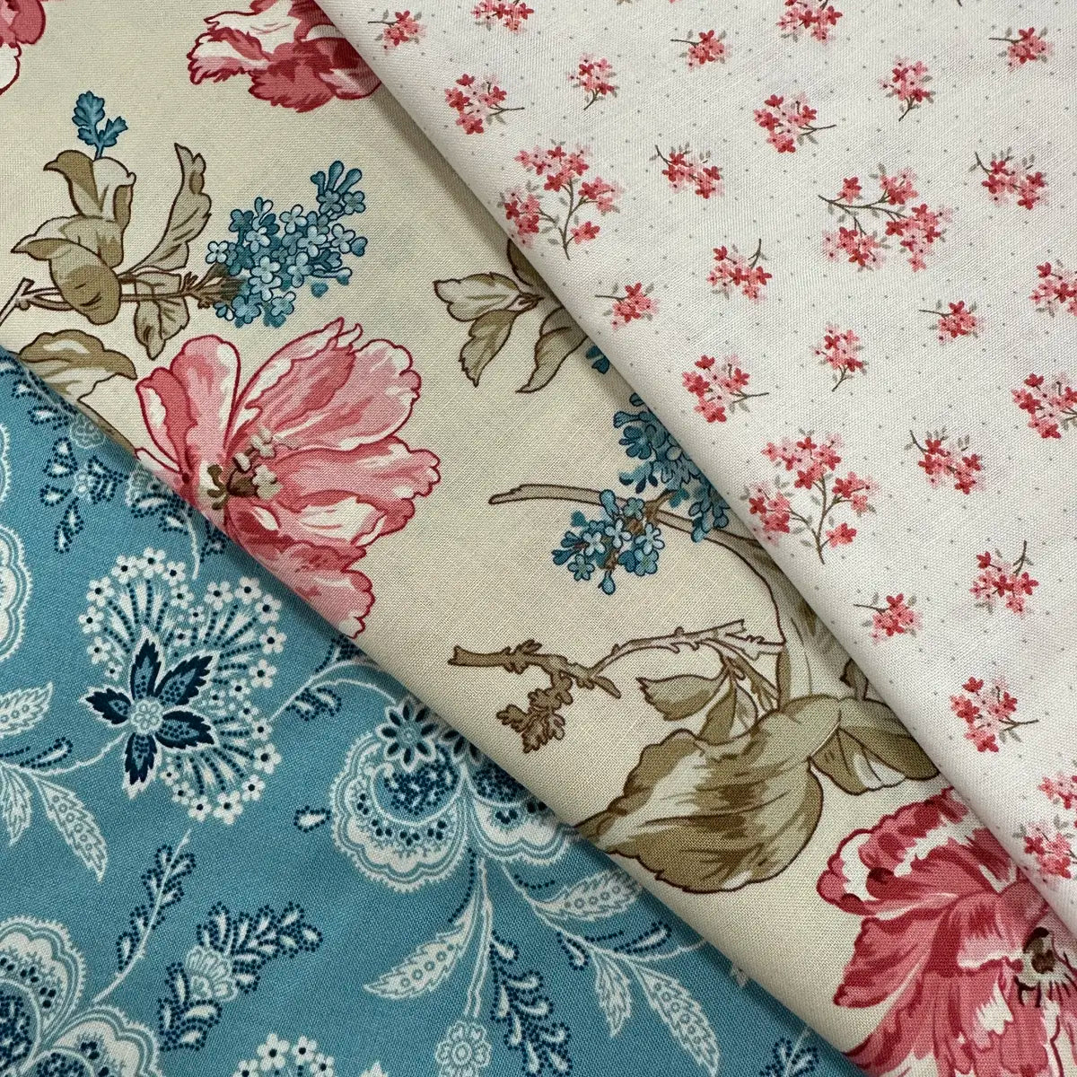 Three pieces of cotton quilt fabric from Quilted Joy are shown in the Lighthouse Front Porch 3 Yard Quilt Top Bundle: a blue and white floral, large pink and beige flowers, and small pink flowers on white—ideal for your next quilt.