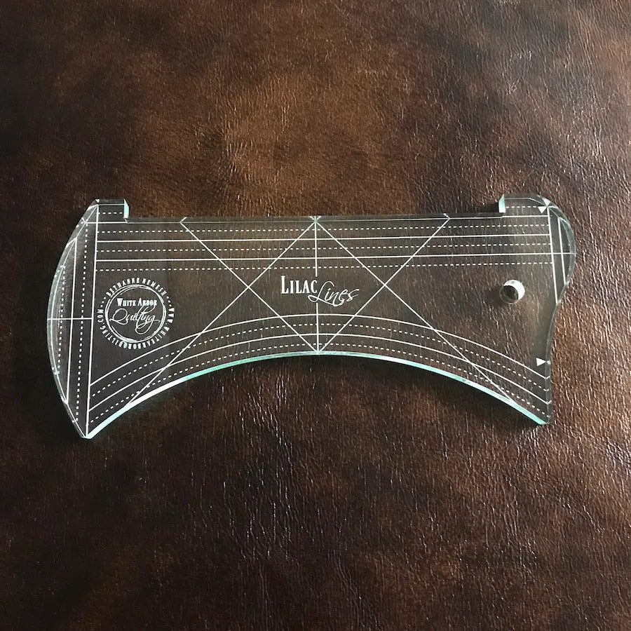 The Lilac & Lavender Duo Ruler Set by White Arbor Quilting features transparent, curved acrylic rulers with dotted lines and logos—ideal for any quilting ruler set, shown here on a brown leather surface.