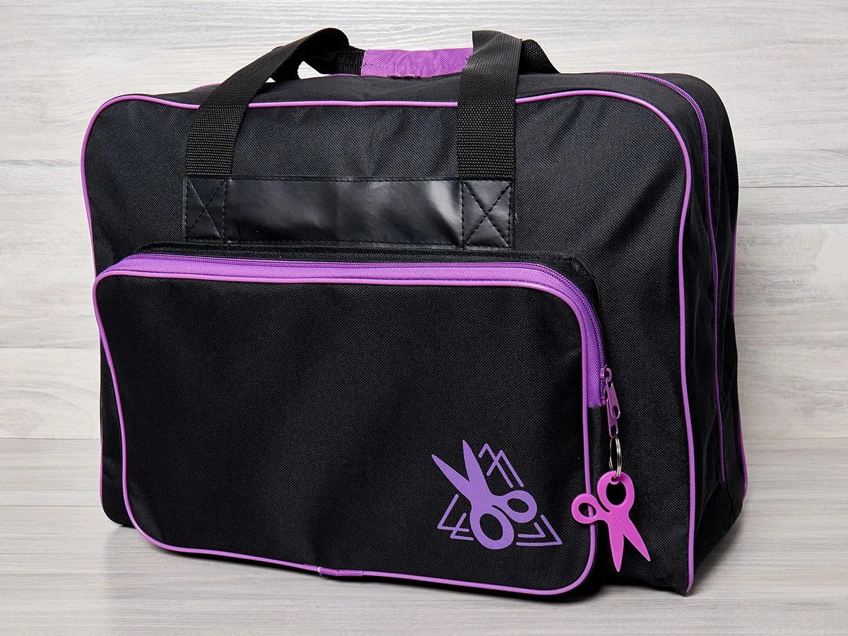 The Tacony Corporation Black Sewing Machine Bag with Purple Accent features purple piping, scissor graphics, a zippered pocket, and padded heavy-duty polyester protection—perfect for machine storage. Two black handles rest on a light wooden surface.