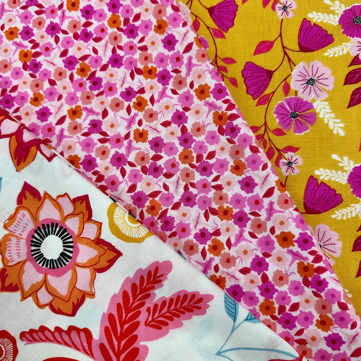 The Memories Unfold 3 Yard Quilt Top Bundle features three cotton fabrics: small pink flowers on white, bold red and orange blooms on light blue, and purple stems on yellow—ideal for projects from Fabric Cafe 3-yard quilt books.