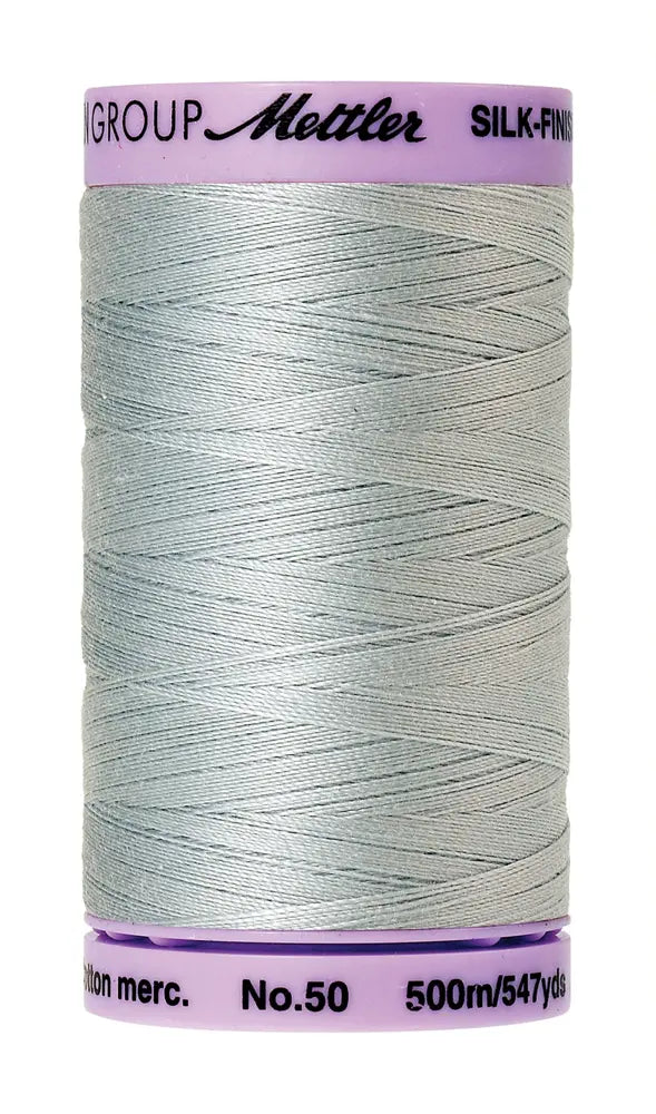 A spool of Mettler Cotton Silk Finish 50wt 500m Moonstone sewing thread, light gray, with a light purple label on top and bottom showing brand and product details.