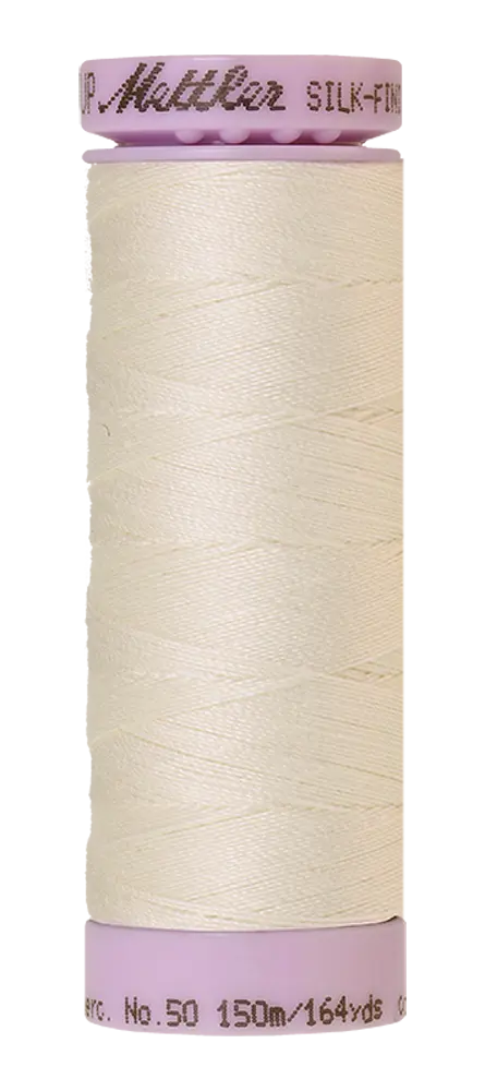 A spool of Mettler Cotton Silk Finish 50wt 150m Muslin off-white thread with light pink ends—ideal for quilting or detailed stitching projects.