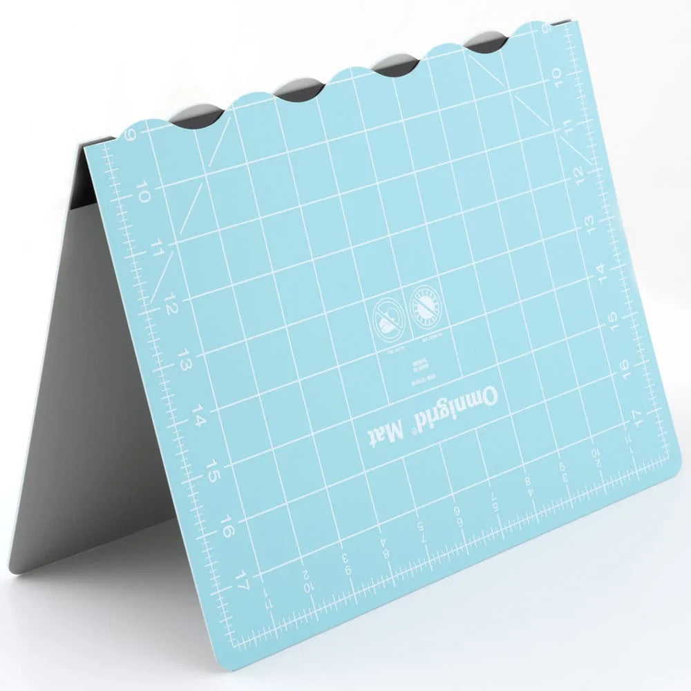 The Tacony Corporation Omnigrid 12 x 18 Compact Rotary Cutting Kit features a blue folding cutting mat standing upright on a gray support, with measured grids, angle markings, and rounded notches along the top edge.