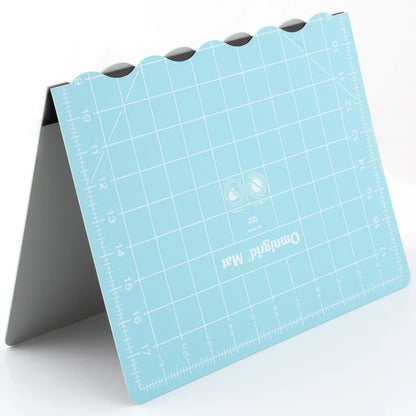 The Tacony Corporation Omnigrid 12 x 18 Compact Rotary Cutting Kit features a blue folding cutting mat standing upright on a gray support, with measured grids, angle markings, and rounded notches along the top edge.