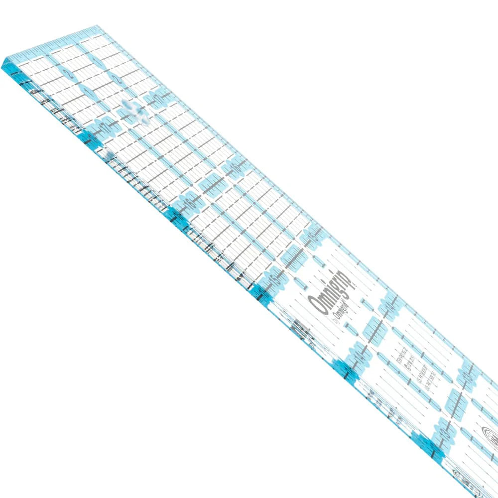 The Omnigrid 12 x 18 Compact Rotary Cutting Kit by Tacony Corporation features a clear quilting ruler with blue grid lines, measurements, and markings—perfect for use with your rotary cutter or folding cutting mat.