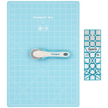 The Tacony Corporation Omnigrid 12 x 18 Compact Rotary Cutting Kit, featuring a blue cutting mat, ergonomic blue-handled rotary cutter, and clear quilting ruler, is displayed side by side on a white background.