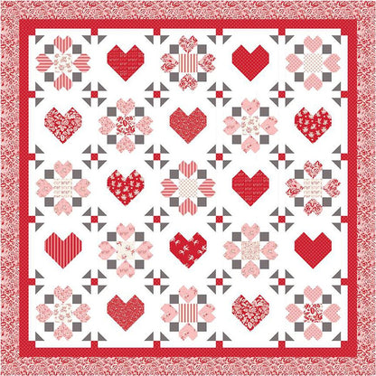 The "Surrounded by Love" quilt pattern by Riley Blake features red and pink hearts and florals in a grid design with a decorative red and white border, and alternating heart and floral blocks on a white background.