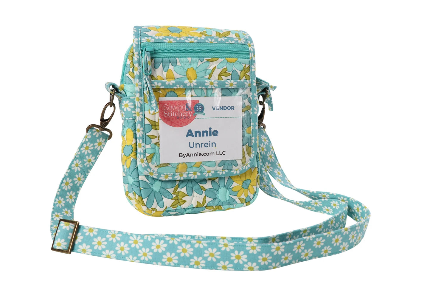 A small quilted crossbody bag made with the On the Go 2.0 Quilt Pattern, featuring a blue/yellow floral design, ByAnnie.com LLC name badge, front zipper pocket, and adjustable strap.