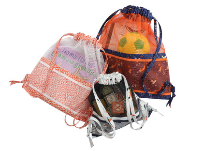 Three colorful mesh bags from the Meshing Around Quilt Pattern by Checker Distributor stand upright with various contents—soccer ball, books, towel—showing their versatility as drawstring backpacks for carrying essentials.