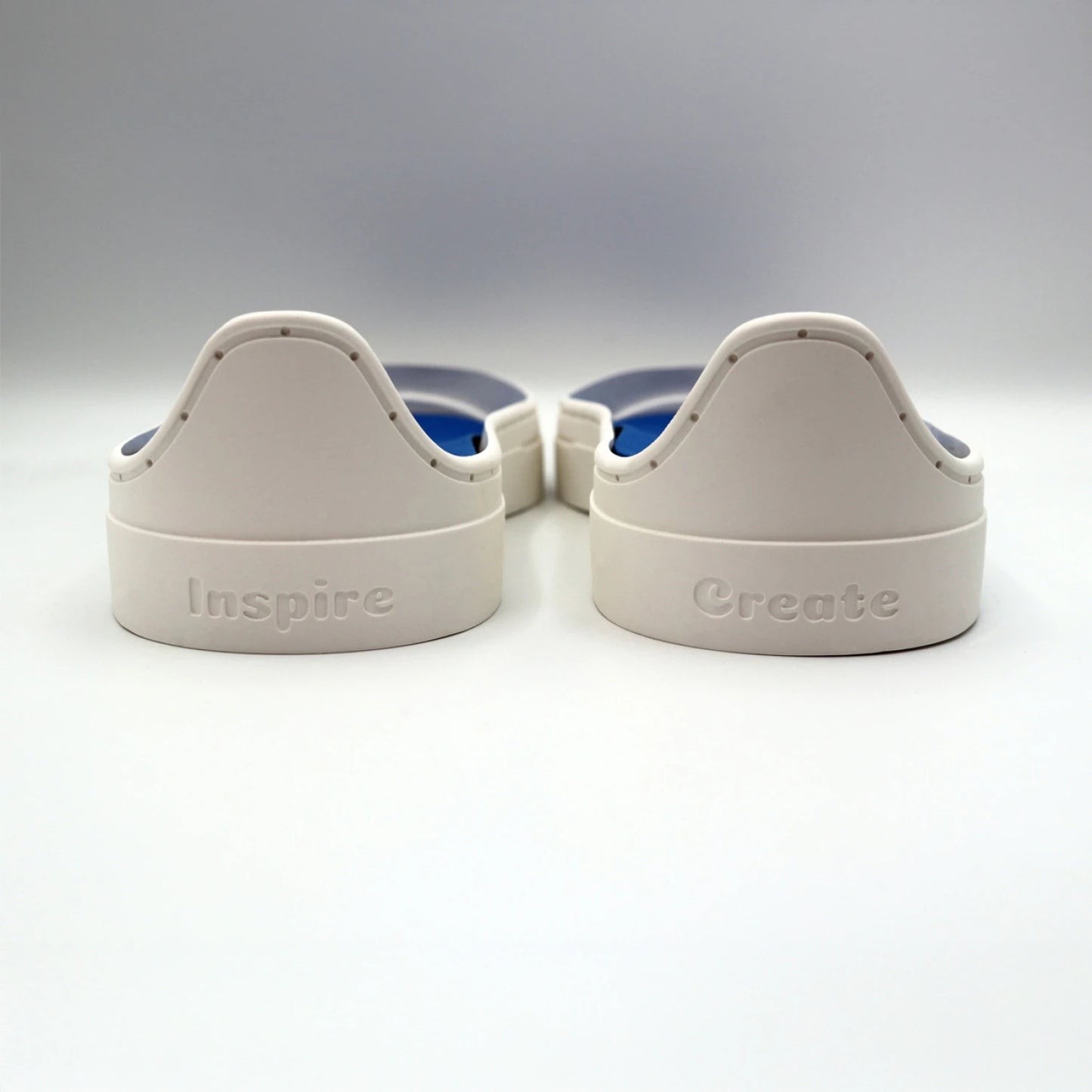 Two white plastic objects from the Patchwork Kicks White Shoe Kit by Checker Distributor sit side by side, labeled "Inspire" and "Create" in raised letters, resembling sneaker components on a white surface.