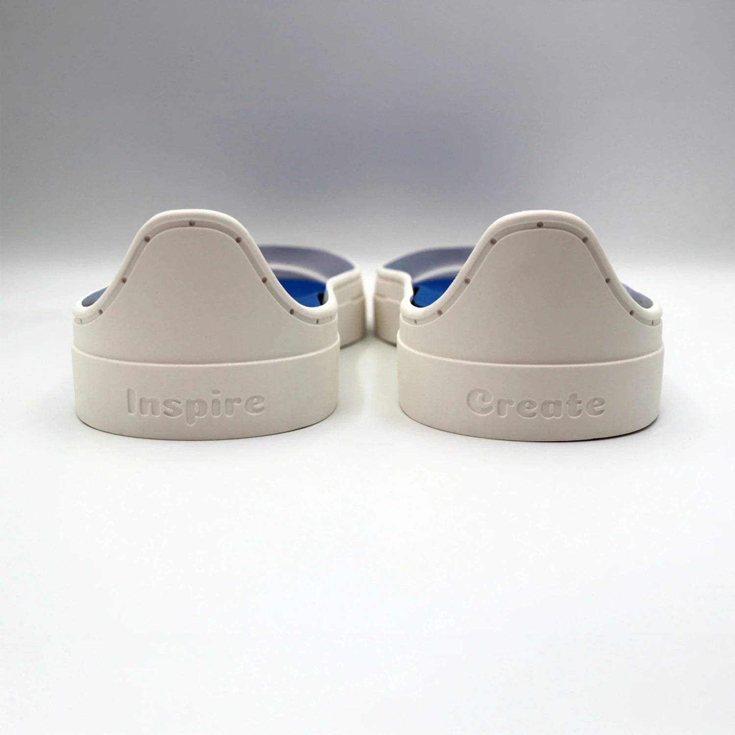 Two white plastic objects from the Patchwork Kicks White Shoe Kit by Checker Distributor sit side by side, labeled "Inspire" and "Create" in raised letters, resembling sneaker components on a white surface.