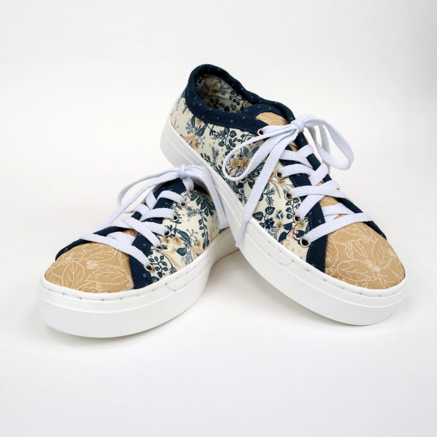 The Patchwork Kicks White Shoe Kit by Checker Distributor features custom sneakers with white soles and laces, tan toe caps, and a blue and cream floral pattern on the uppers, shown against a plain white background.